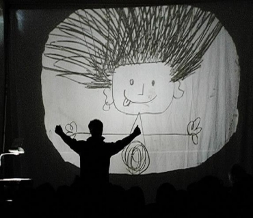 Gek Tessaro che disegna la figura di un bambino su una lavagna luminosa